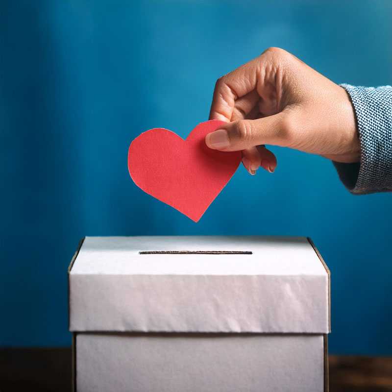 A hand placing a paper heart into a ballot box