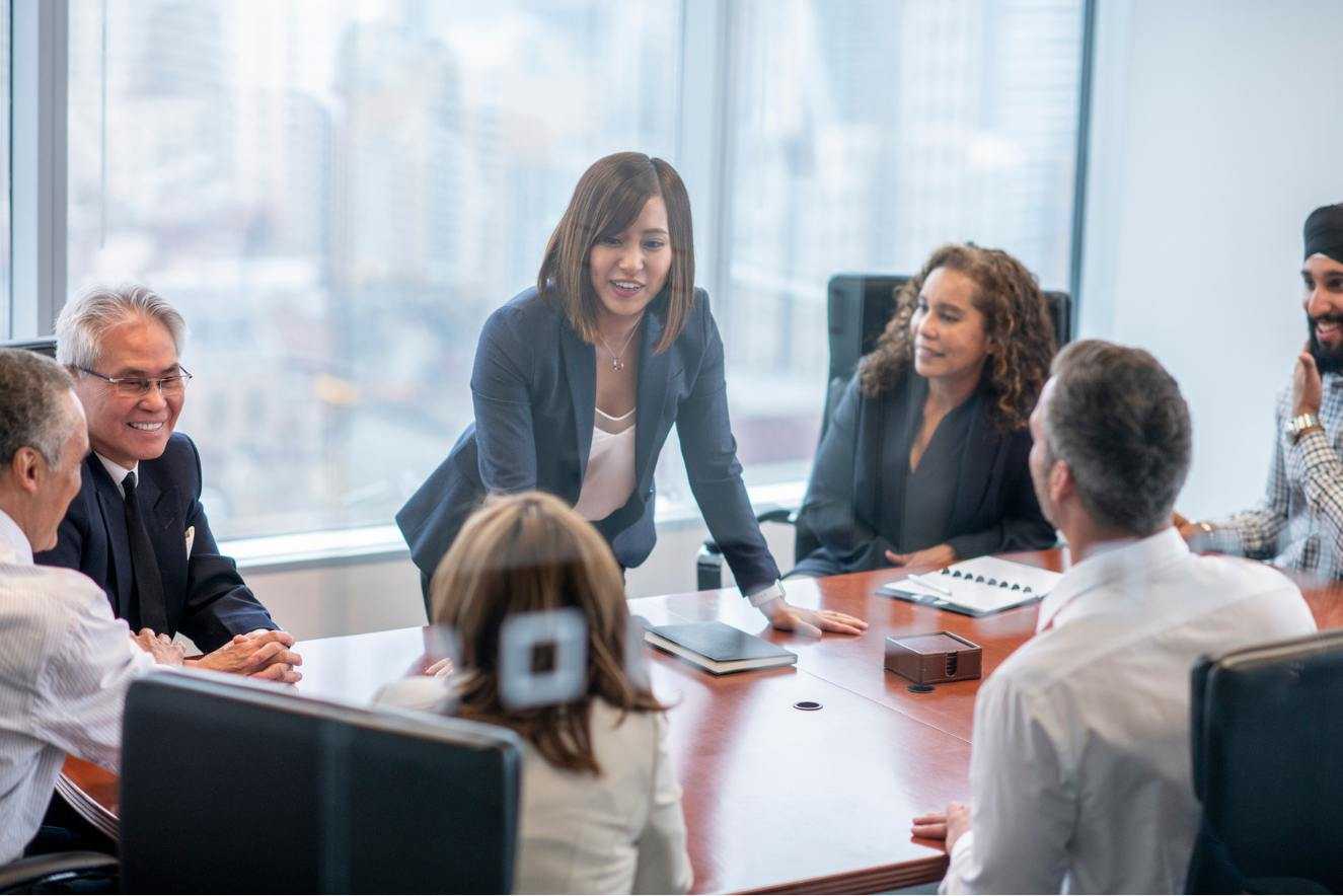 Multicultural leaders smile around a board room table.