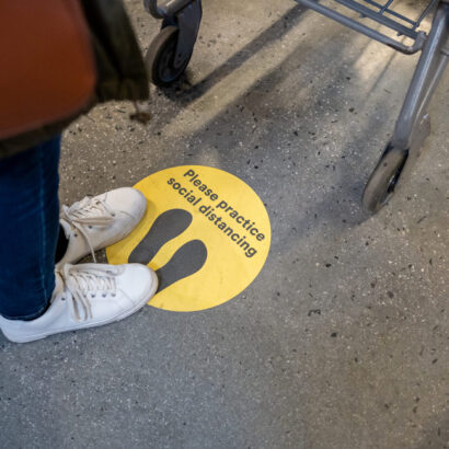 Person standing on label on floor asking to practice social distancing